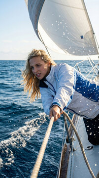 A focused woman pulls a rope aboard a sailboat at sea, capturing active sailing, teamwork, ocean adventure, and determined effort under bright wind-filled sails.