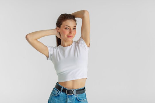 Young woman smiles softly with arms raised behind her own head, elegance that needs no extra detail, clean line and calm colour. Wide shot. Concept of elegance of simple cotton basic