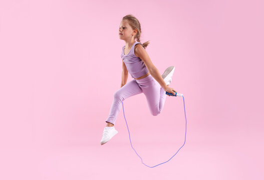 Cute little girl jumping with skipping rope on pink background
