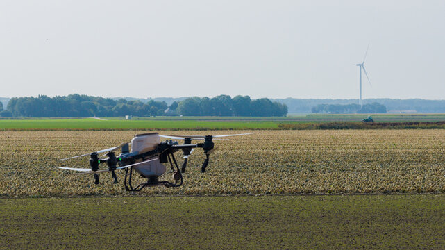 Aerial view of an agricultural drone flying over a cultivated field with a wind turbine in the distance in Zeewolde, Flevoland, Netherlands.