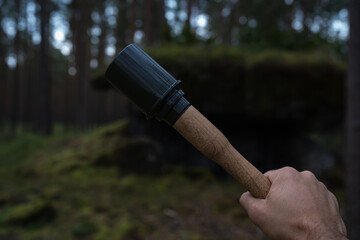 Obraz premium ​A close-up photograph of a hand holding a wooden and 3D printed replica of a WWII German Stielhandgranate stick grenade in a deep forest.