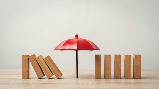 Red umbrella protects standing wooden dominoes from falling during a conceptual insurance demonstration on light wooden surface background for business