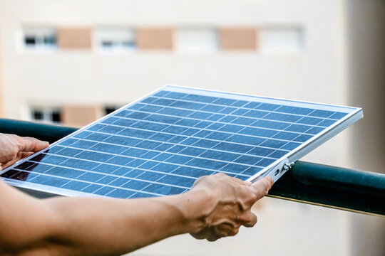 Woman holding small solar panel on apartment balcony for residential renewable energy and sustainable electricity