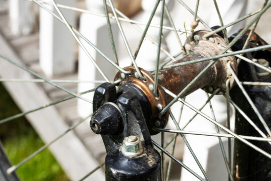 Weathered bicycle wheel hub, axle hardware and crossed metal spokes in close up detail, showing rusty aged mechanical texture, circular engineering component and utilitarian bike repair character
