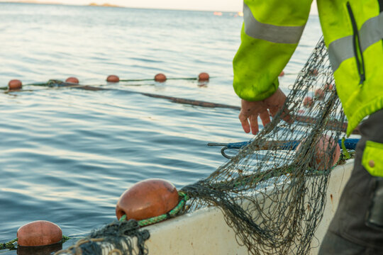 Fisherman handling traditional fishing net from small coastal boat.