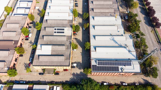 Aerial view of an industrial and logistics zone with large warehouses, solar panels on rooftops, and parked vehicles in Milan, Lombardy, Italy.