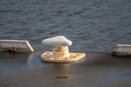 Minimalist dock bollard detail with rust texture and blue water background.