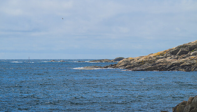 Rocky coastal seascape with dark water and cloudy horizon.