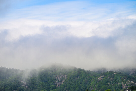 Low clouds drifting over forested rocky mountain slopes.