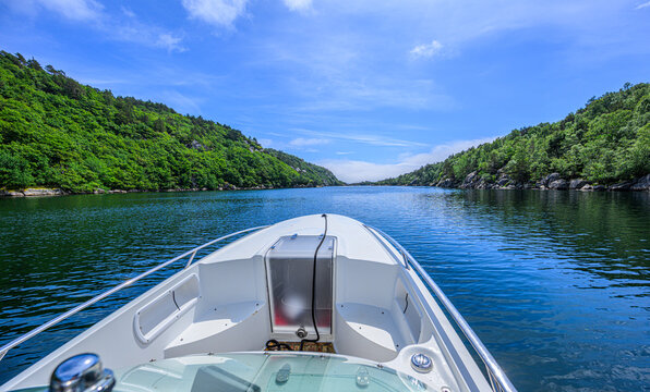 Bow of speedboat cruising through calm forested fjord.