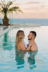 Fototapeta premium Romantic couple embracing in an infinity pool at sunset, luxury tropical resort with panoramic ocean view, honeymoon travel and vacation concept, high quality photo