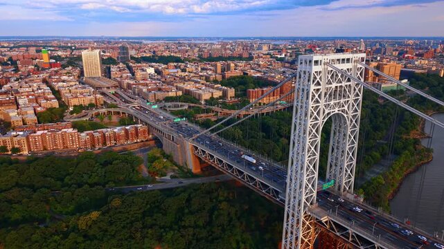 George Washington Bridge tower beside Manhattan apartment blocks. Traffic crosses the steel span above a wooded riverbank with dense housing beyond.