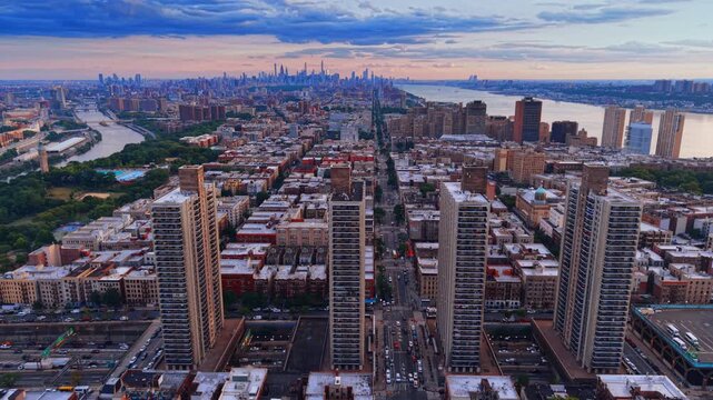 Upper Manhattan apartment towers and avenues at dusk. Rows of rooftops and residential towers extend toward the skyline between two rivers.