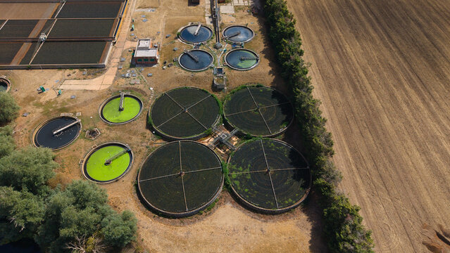 Aerial view of the wastewater treatment works featuring circular sedimentation tanks and filtration basins surrounded by agricultural fields in St Neots, England, United Kingdom.