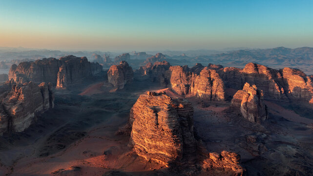Drone aerial view of dramatic sandstone rock formations illuminated by golden sunrise light in AlUla desert