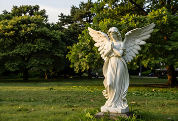 Obraz premium Spirituality and peace concept, white stone angel statue with praying hands in a serene park garden setting during golden hour sunlight for memorial