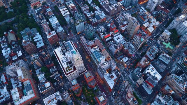 Overhead view of Manhattan streets and rooftops. Intersecting streets divide dense city blocks with flat roofs, vehicles and tree canopies.