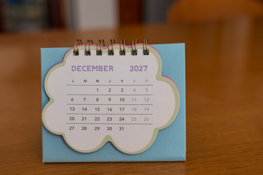 December 2027. Image of a pastel-colored desk calendar placed on a wooden desk.