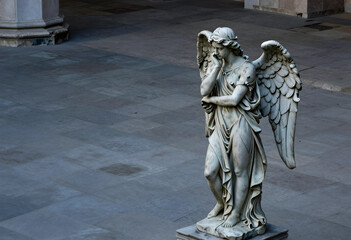 Obraz premium Grief and mourning concept, stone angel statue with wings standing in a pensive pose in a quiet courtyard for funeral or memorial service themes