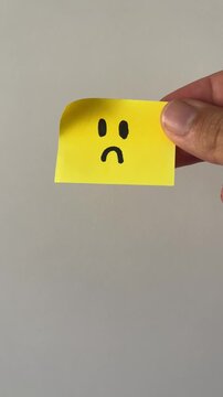 Hand holding sad face sticky note on gray background
