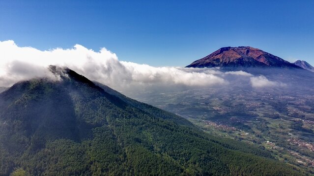 Aerial view of Mount Telomoyo with lush green slopes, rolling hills, and clouds drifting over the volcanic landscape in Kecamatan Ngablak, Jawa Tengah, Indonesia.