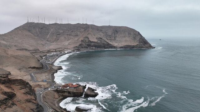 Aerial view of the rugged coastline and cliffs of the Morro Solar area with a winding coastal road and the Pacific Ocean waves crashing against the shore in Barranco, Lima Province, Peru.