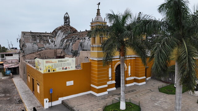 Aerial view of the historic Iglesia La Ermita de Barranco with its distinctive yellow facade and damaged roof structure, surrounded by palm trees in Barranco, Lima Province, Peru.