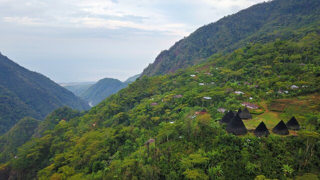 Panoramic drone shot of isolated Wae Rebo village surrounded by mist covered mountains