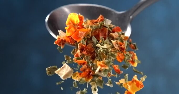 Dried herbs and spices falling from a spoon in slow motion on blue background