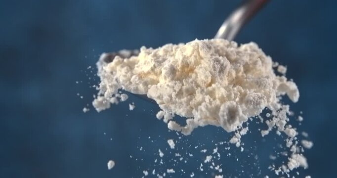 Flour falling from a spoon in slow motion on blue background