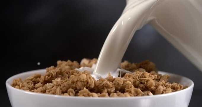 Milk pouring onto granola in bowl for breakfast in slow motion close up