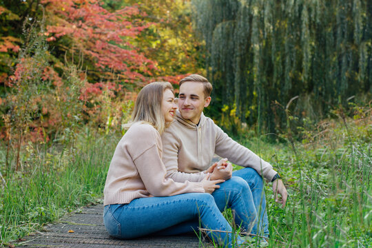 Young happy Caucasian couple in love holding hands and enjoying the moment during romantic walk on nature in the fall park. Autumn mood. Youth feelings and first love emotions concept.