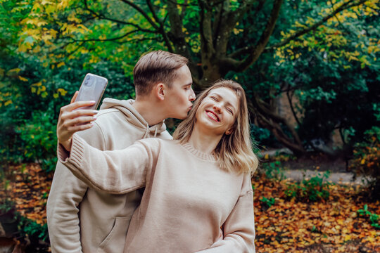 Young friends or couple in love doing selfie by phone while enjoys time together during romantic walk in nature in the fall park. Autumn mood. Youth feelings and first love concept. Students have fun.