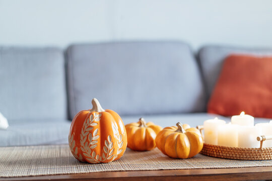 Cozy warm autumn home interior - decorative orange ceramic pumpkins, candles on the wooden coffee table and gray sofa with bright cushions on background . Scandinavian minimalist hygge home fall decor