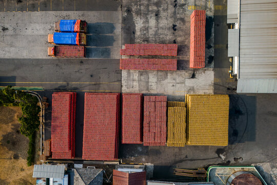 Aerial view of stacks of red and yellow plastic crates arranged in a warehouse yard with trucks parked nearby in Semarang Regency, Central Java, Indonesia.