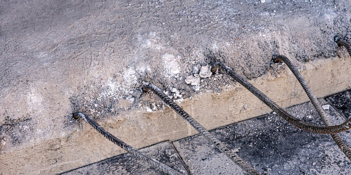Detail close-up of a textured concrete slab featuring protruding rusted steel reinforcement bars. The scene captures the raw essence of construction or structural engineering.