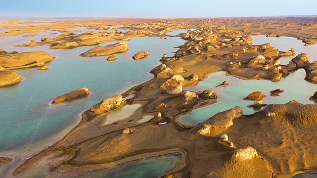 High angle wide shot reveals yardang landforms surrounded by clear turquoise water in Qinghai, captured during bright day.
