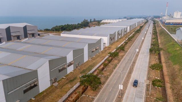 Aerial view of Kawasan Industri Terpadu Batang featuring large industrial warehouses and a long road stretching along the coast in Kecamatan Gringsing, Jawa Tengah, Indonesia.