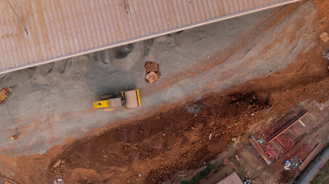Aerial view of Kawasan Industri Terpadu Batang with a yellow road roller compacting gravel and soil at a construction site in Kecamatan Gringsing, Jawa Tengah, Indonesia.