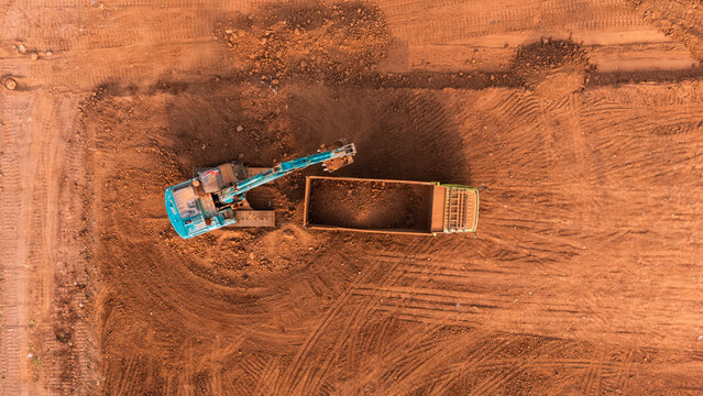 Aerial view of an excavator loading soil into a dump truck at the Kawasan Industri Terpadu Batang construction site in Kecamatan Gringsing, Jawa Tengah, Indonesia.