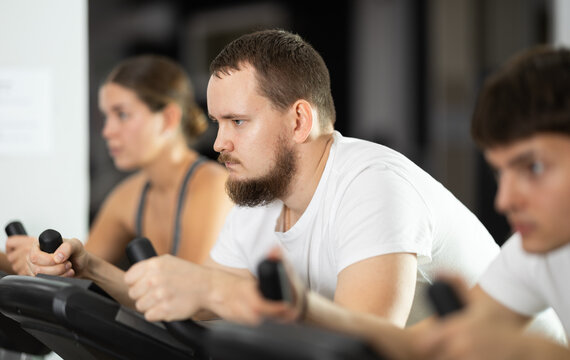 Bearded man hardly perform exercise on stationary bicycle, pedaling and exercising in fitness class. Fitness equipment, visitors engaged in physical task during training