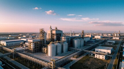 Fototapeta premium Aerial view of massive industrial factory complex at sunset. Large manufacturing plant with metal silos, pipes, warehouses, production buildings. Huge logistics zone for economic development, heavy