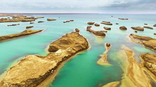 High angle shot shows unique yardang landforms surrounded by turquoise water under a cloudy sky in Qinghai.