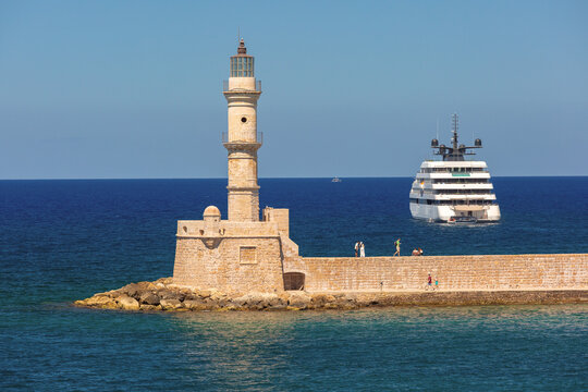 Historic Chania Lighthouse on the harbor breakwater with a luxury yacht sailing in the Mediterranean Sea in Chania, Crete, Greece.