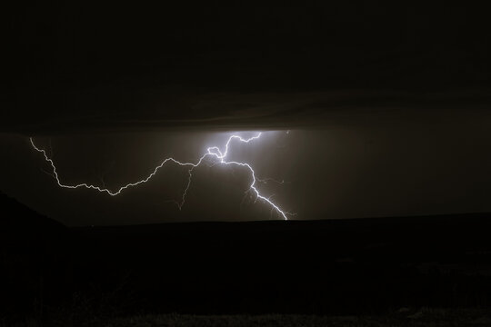 Rayo ramificado iluminando intensamente el cielo nocturno nublado sobre un horizonte oscuro en una tormenta el&eacute;ctrica.