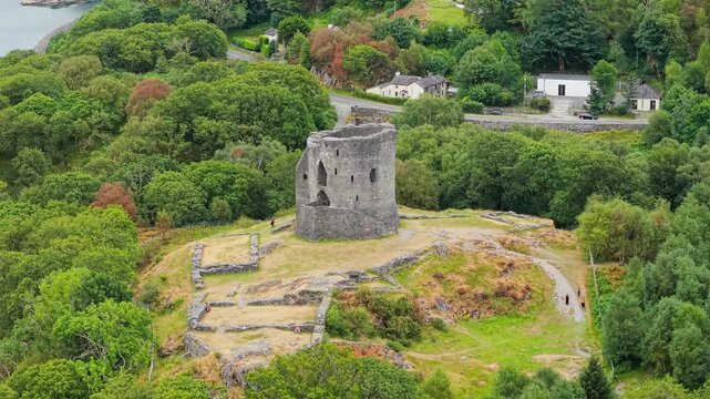 Aerial view of Dolbadarn Castle stone tower standing on a grassy hill above Padarn Lake, surrounded by green woodland in Llanberis, North Wales