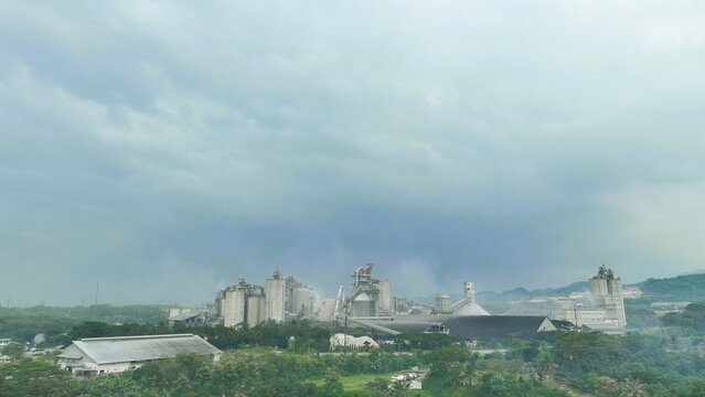 Aerial view of the Nambo cement factory featuring large industrial silos, processing structures, and chimneys surrounded by lush tropical greenery in Klapanunggal, West Java, Indonesia.
