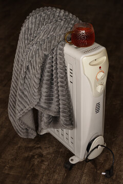 Tea cup, blanket lie on an electric radiator. Indoor winter lifestyle, domestic heating, energy crisis, comfort concept