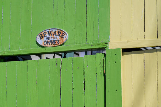Closeup of "Beware of the Owner" Sign on Front of Green Wooden Gate 