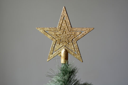 Close up of sparkling golden star on top of Christmas tree against flat neutral wall